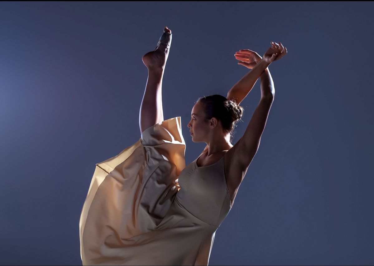 zur Vergrößerungsansicht des Bildes: Balletttänzerin vor neutralem schlichten Hintergrund, ein Bein und die Arme sind im Tanz nach oben gestreckt.